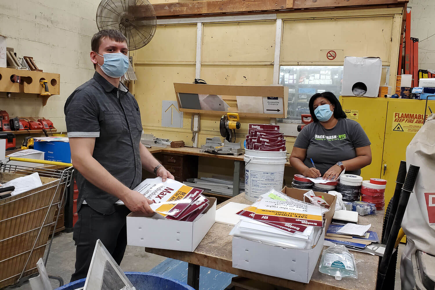 Julissa Lora, Environmental Health and Safety Sustainability Coordinator, and Victor Buzin, EHS Coordinator, sort through boxes of newly printed signage. These signs were installed on walls, floors, hallways, elevators, and gates in preparation for re-entry.