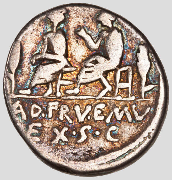 The reverse (back) of the Roman Republic denarius shows two seated quaestors—flanked by sheaves of wheat—representing L. Calpurnius Piso Caesoninus and Q. Servilius Caepio—Roman officials who had charge of public revenue and expenditure who issued the coin. The abbreviation AD·FRV·EMV EX·S·C stands for Ad frumentum emundun ex senatus consulto, “for the purchase of grain by order of the senate.”